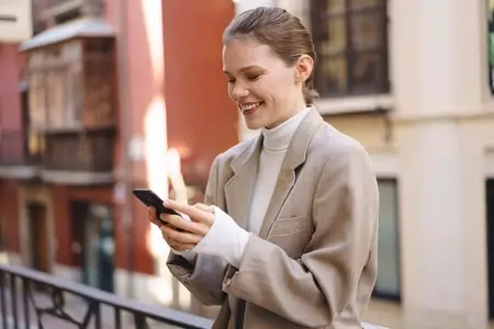 A Happy and Smiling Woman Engaged Deeply with Her Smartphone in a Lively Urban Setting