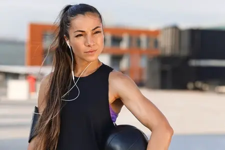 Confident female athlete with medicine ball wearing headphones  Portrait of a young woman relaxing with medicine ball during workout