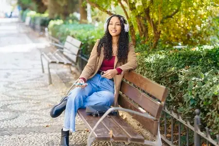 A Young Woman Happily Enjoys Listening to Music While Sitting in a Beautiful Park Setting