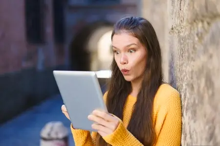 A Surprised Young Woman Engaged with Her Tablet While in an Urban Setting Filled with Life