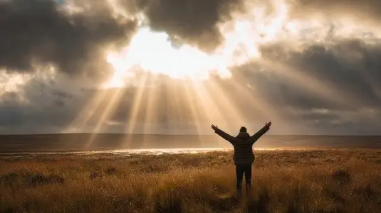 Person standing in wide open field with arms raised  embracing sunlight breaking through clouds  radiating joy and freedom