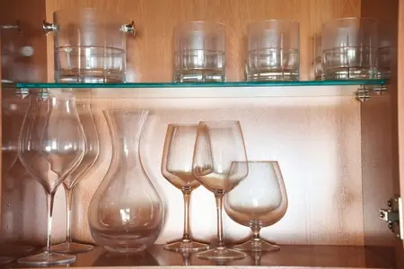 Luxurious glass collection showcased with soft amber illumination  Sophisticated assortment of crystal glasses accentuated by warm backlighting against textured