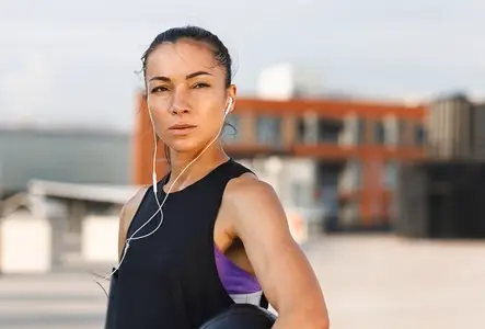 Portrait of a young confident female in headphones  standing on the roof and holding medicine ball