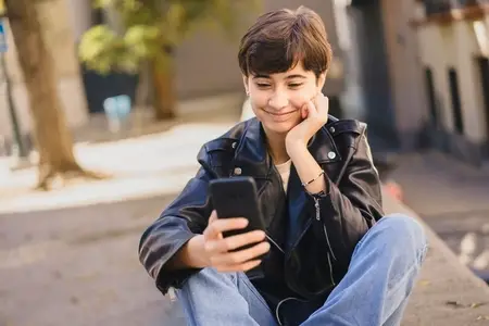 A joyful teenager is engaged with their smartphone while enjoying the outdoors today