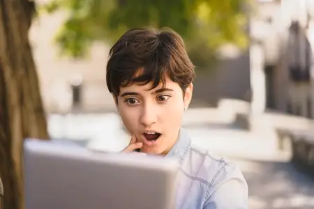A Surprised Young Woman is Engaged Enthusiastically with Her Laptop While Outdoors