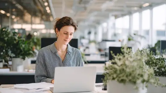 Focused employee working modern office desk with laptop surrounded by plants and natural light creating productive Focused employee working modern office desk with laptop surrounded by plants and natural light creating productive