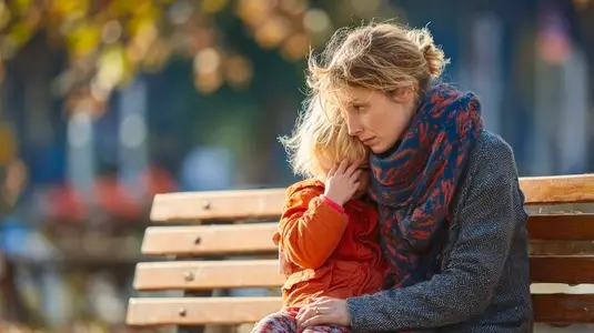 Mother comforting child park bench  emotional moment captured  warm autumn colors  candid scene  connection between parent